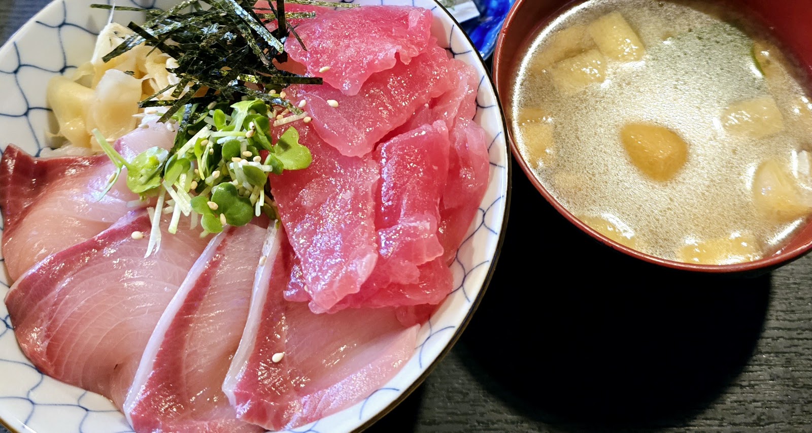 白い丼にのせた鮪の赤身とぶり、刻み海苔とかいわれ。横に麩の入った赤い椀の汁物。